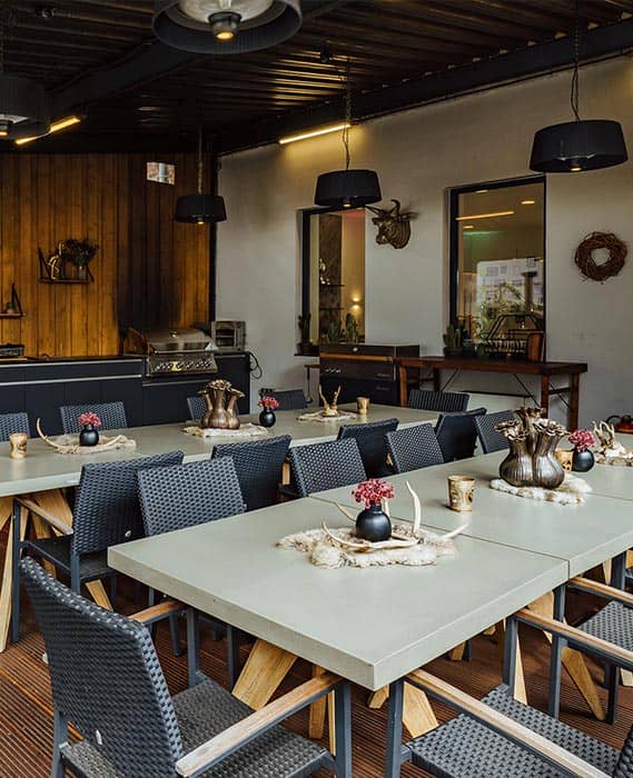 Gemütlicher, überdachter Außenbereich mit Grill und rustikal dekorierten Tischen vor Halle 22 im Grillfachgeschäft Düsseldorf